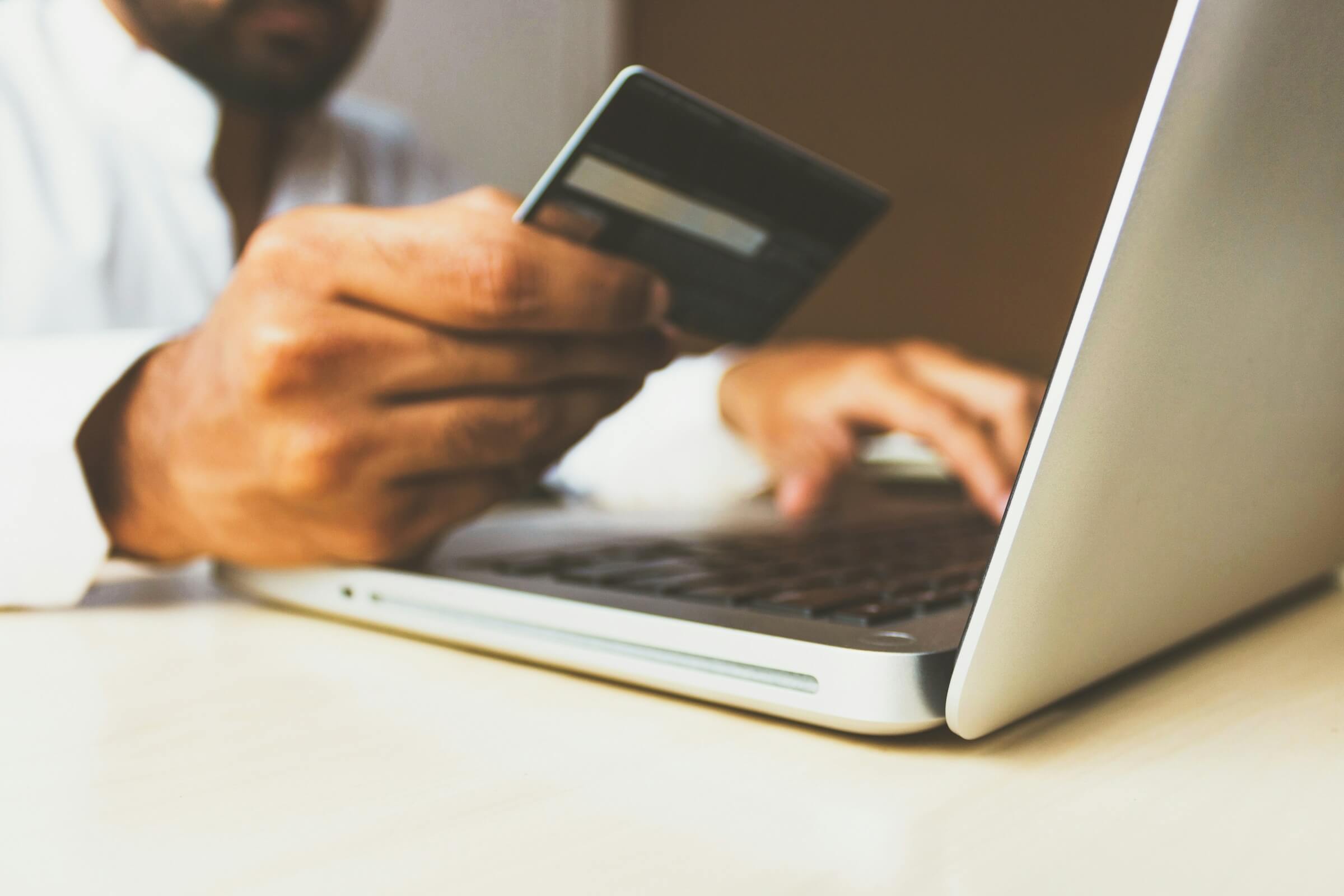 A man looking at his credit card while using a laptop