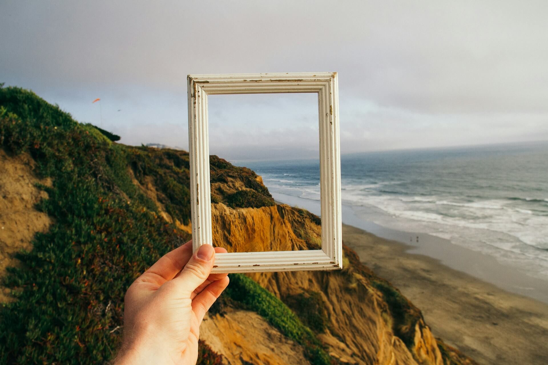 A person holding an empty picture frame overlooking a beach view